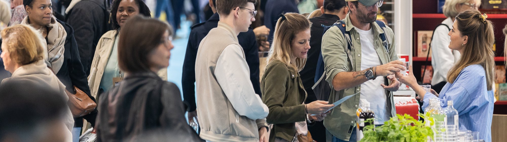 Groupe de visiteurs échangeant avec une exposante sur un stand lors d’un salon professionnel.
